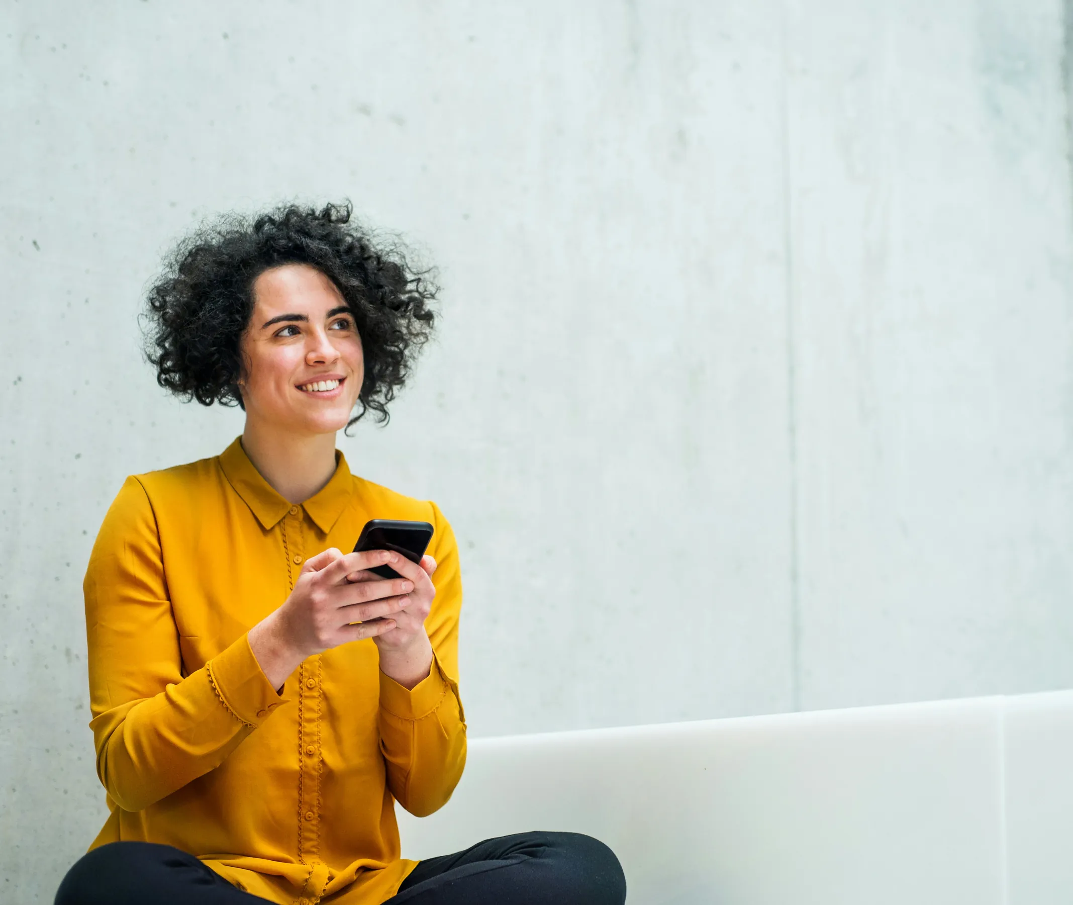 A woman sitting cross-legged, smiling as she checks her phone