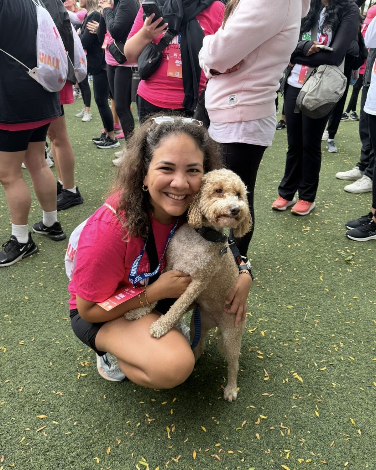 Malak crouching on a field at a charity walk, smiling with her arms around a curly-haired dog